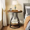 A round side table with a lamp, alarm clock, and teacup on top, placed next to a bed. Produktbild-Vorschau