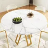 A round marble-effect dining table with gold legs, set with a bowl of green fruit and a decorative tray, surrounded by white chairs in a brightly lit room with a patterned rug. Podgląd zdjęcia produktu