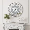 A large wall clock with Roman numerals is mounted on a wall above a decorative fireplace mantel. The mantel displays a vase of greenery and a silver horse sculpture. Anteprima dell’immagine prodotto