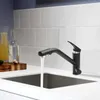 A black kitchen faucet with water running into a sink, with bottles and a cutting board in the background. Produktbild-Vorschau