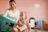 A woman is reading a book to a baby in a room with pink walls and stuffed penguins. Produktbild-Vorschau