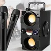 A portable Bluetooth speaker with two microphones, set against a blurred background of people playing music. Podgląd zdjęcia produktu