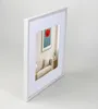A white picture frame with a mat and a picture of a red poppy in a living room setting. Produktbild-Vorschau