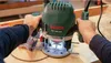 Hands holding a Bosch router over a piece of wood. Anteprima dell’immagine prodotto
