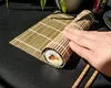 A hand is shown rolling a sushi roll on a bamboo mat. Náhľad obrázku produktu