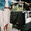 A person is holding a stroller handle with a black diaper bag attached. Produktbild-Vorschau