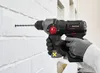A hand wearing a glove is using a cordless drill to drill a hole in a white brick wall. Produktbild-Vorschau