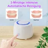 A hand is pressing a button on a white ultrasonic cleaner. Above the cleaner are two images of dentures, one labeled 'Vorher' (Before) and the other 'Nachher' (After). Text at the top reads '3-Minütige intensive Automatische Reinigung'. Produktbild-Vorschau