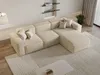 A modern beige sectional sofa in a well-lit living room with a rug and shelves in the background. Produktbild-Vorschau