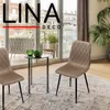 Two beige chairs are placed around a small glass-topped table with green vases on it, in a room with large windows overlooking a city. Produktbild-Vorschau