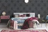 A bedroom scene with a bed, nightstand, chair, and rug, showcasing the wallpaper. Produktbild-Vorschau