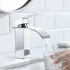 A modern chrome faucet is filling a glass of water on a white countertop. Produktbild-Vorschau