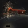 A decorative LED tree is shown in a snowy outdoor setting at night, with a red building in the background. Náhled obrázku produktu