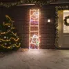 A festive outdoor scene with a decorated Christmas tree and a lit-up LED silhouette of Santa Claus on a ladder, set against a brick wall and snowy ground. Produktbild-Vorschau