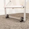 Close-up of the lower part of a ladder, showing its wheels and support bar on a carpeted floor. Produktbild-Vorschau
