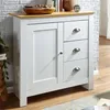 A white sideboard with a wooden top and three drawers, set against a white brick wall. Podgląd zdjęcia produktu