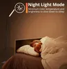 A child sleeping in bed with a teddy bear, illuminated by a floor lamp. Produktbild-Vorschau