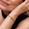 Close-up of a woman's arm wearing a gold charm bracelet. Podgląd zdjęcia produktu