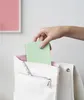 A hand is placing a green notebook into a white backpack. Anteprima dell’immagine prodotto