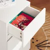 A close-up view of an open drawer in a white cabinet, revealing a red book with black glasses on top. Náhľad obrázku produktu