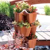 A tiered planter filled with red and green plants sits on a wooden deck next to a body of water. Náhľad obrázku produktu