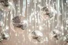 Several shiny silver disco balls hanging from strings against a background of vertical silver tinsel. Produktbild-Vorschau