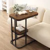 A small side table with two shelves next to a sofa, holding a book, a vase with greenery, and a cup. Produktbild-Vorschau