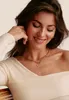 A woman wearing a white top and a gold necklace with a heart pendant. Voir les images du produit