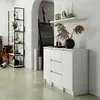 A white dresser with three drawers and two doors is shown in a room with an easel and artwork in the background. Podgląd zdjęcia produktu