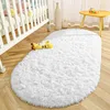 Weißer flauschiger ovaler Teppich auf hellem Holzboden in einem Kinderzimmer, neben einem weißen Kinderbett und einem gelben Giraffen-Spielzeug Náhled obrázku produktu