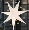 A white, star-shaped paper lantern with small star cutouts is illuminated from within, hanging in front of a window with blurred lights. Podgląd zdjęcia produktu