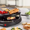 A raclette grill with food being cooked on it, set on a table with bread and vegetables. Anteprima dell’immagine prodotto