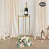 A gold rectangular flower stand with a bottle of champagne and two glasses on top, set against a backdrop of cream-colored curtains. The base of the stand is adorned with a floral arrangement. Podgląd zdjęcia produktu