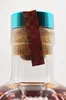 Close-up of the top of a bottle, showing the cork, cap, and a decorative band. Produktbild-Vorschau