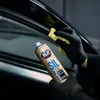 A person wearing black gloves is cleaning a black surface with a yellow cloth and a spray can. Produktbild-Vorschau