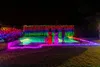 A backyard swimming pool area decorated with numerous colorful LED string lights at night. Náhled obrázku produktu