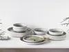 A set of ceramic dishes and bowls are arranged on a white surface against a white wooden wall. Náhľad obrázku produktu