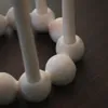 A close-up view of a white candle holder with spherical elements and cylindrical stems, resting on a dark wooden surface. Produktbild-Vorschau