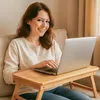 A woman is sitting on a couch using a laptop on a portable table. Podgląd zdjęcia produktu