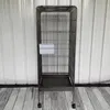 A tall, dark gray bird cage with wheels is shown in front of a corrugated metal wall and a wooden floor. Náhled obrázku produktu