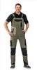 A man wearing olive and black overalls and a black polo shirt stands against a white background. Produktbild-Vorschau