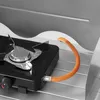 A close-up view of a portable camping stove with an orange gas hose connected to it. Produktbild-Vorschau