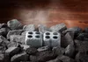 Two stone cubes with four holes each, surrounded by sauna stones, with steam rising in the background. Produktbild-Vorschau
