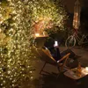 A person relaxing in a hammock chair at night, illuminated by string lights, while looking at their phone. A bicycle and a small table with drinks are visible in the background. Produktbild-Vorschau