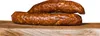 Two sausages are stacked on a wooden board against a white background. Produktbild-Vorschau