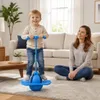 Junges Kind spielt fröhlich mit einem blauen Pogo-Ball im Wohnzimmer, während eine erwachsene Frau zuschaut Podgląd zdjęcia produktu
