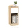 A light wood bedside table with a white drawer and shelf, featuring a plant, mug, and phone on top, and books on the shelf. A white cable is visible. Náhled obrázku produktu