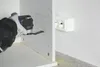 A person is using a power tool to cut a hole in a white cabinet, with electrical outlets visible on the wall. Podgląd zdjęcia produktu