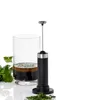 A handheld electric frother is positioned in front of a glass of dark liquid with green herbs, next to a pile of chopped herbs. Produktbild-Vorschau