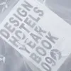 A white sheer curtain with embroidered leaves is draped over a book titled "DESIGN HOTELS YEAR BOOK 0903". Produktbild-Vorschau